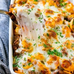 A pan of cheesy baked tortellini with a spoon lifting up a portion.