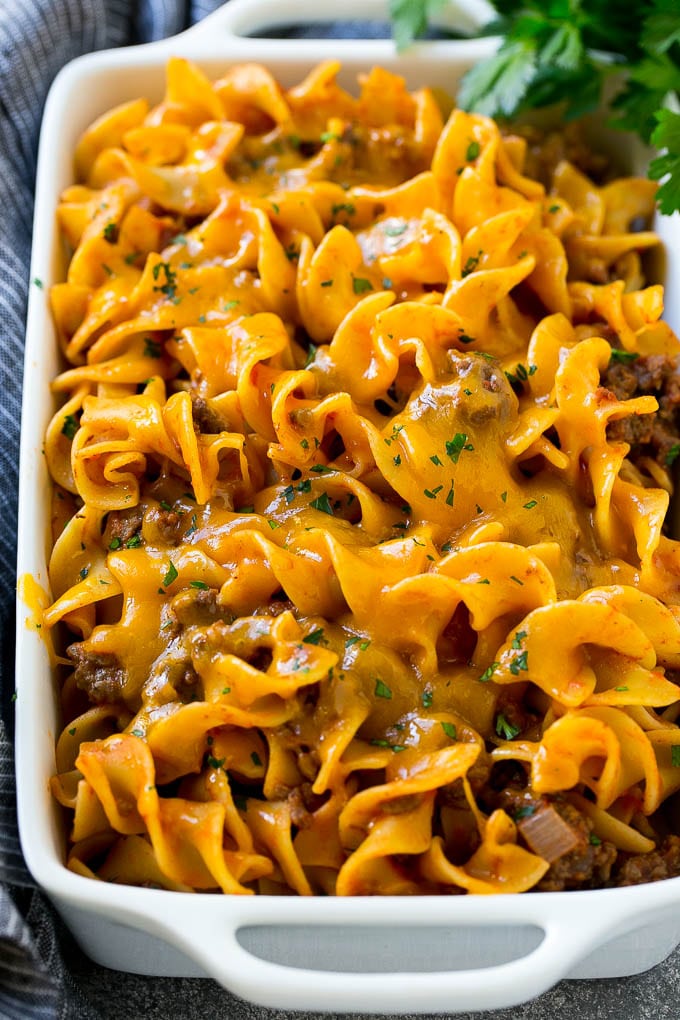 Beef noodle casserole in a serving dish topped with melted cheddar cheese and parsley.
