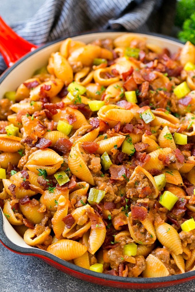 A pan of pasta with ground beef, onion, pasta shells, cheddar cheese and bacon.