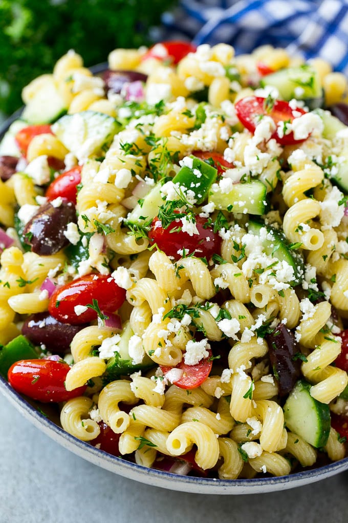A bowl of Greek pasta salad loaded with feta cheese, olives, tomatoes, cucumber and bell peppers.
