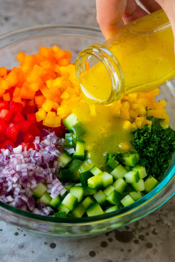 Lemon dressing being poured over chopped vegetables.
