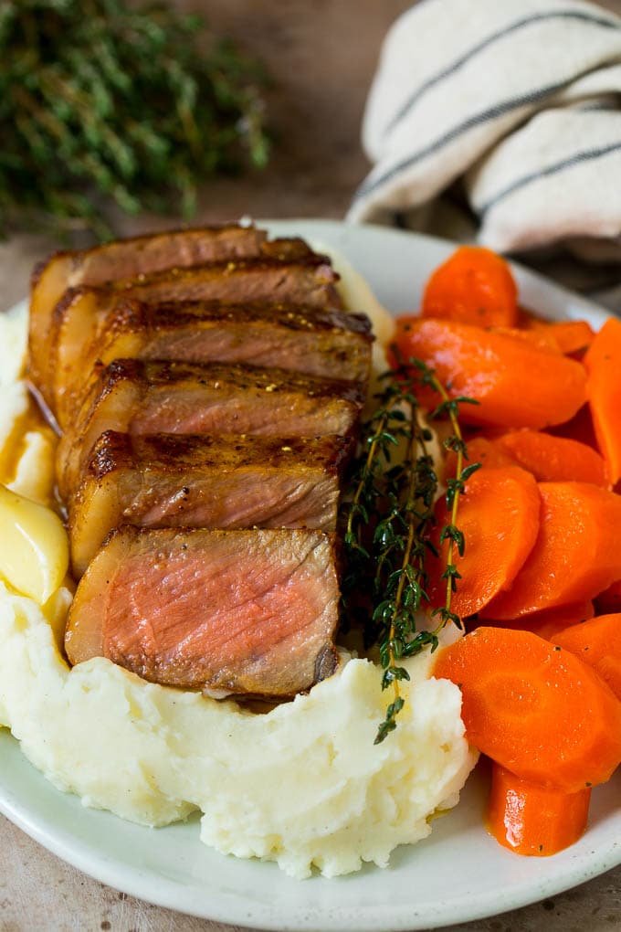 Sliced New York strip steak served with mashed potatoes and carrots.