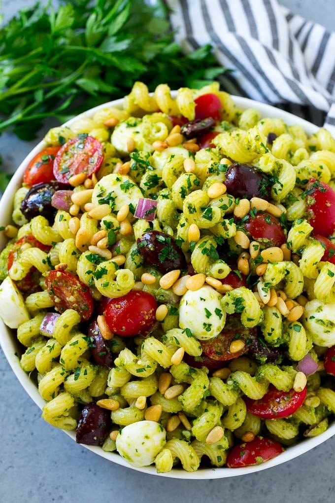 A bowl of pesto pasta salad topped with pine nuts and chopped parsley.