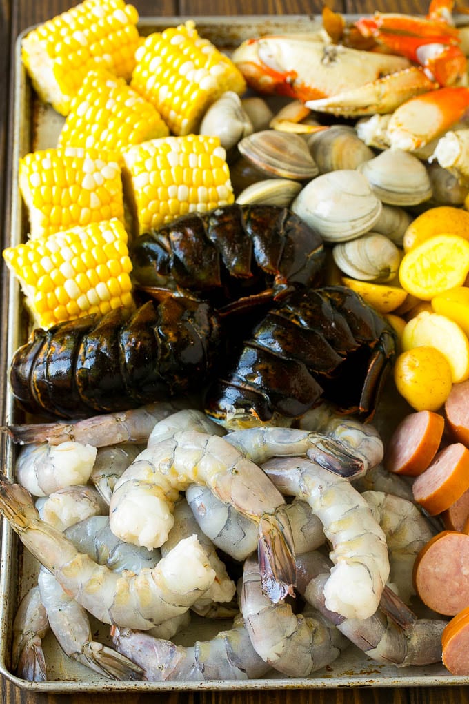Raw shrimp, lobster, sausage, corn, clams and potatoes on a sheet pan.